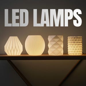 May include: Four white LED lamps with unique geometric designs are displayed on a wooden shelf. The lamps are lit, showcasing their intricate patterns. The text "LED LAMPS" is above the lamps.