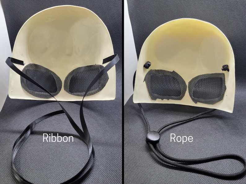 May include: A cream-colored mask with black mesh eye coverings. The mask has a curved shape and is shown with a black ribbon and a black rope. The word "Ribbon" is written on the image.