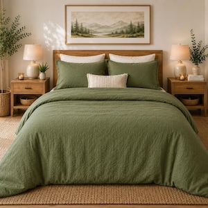 May include: A bed with olive green bedding, including a comforter and pillowcases. The bed is made up with a neutral-toned rug and wooden nightstands with lamps. A landscape painting hangs above the bed, and a woven basket with a plant is on the left.