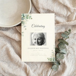 Könnte beinhalten: Eine rechteckige Gedenkprogrammkarte mit einem schwarz-weißen Porträt einer Person. Der Text lautet Celebrating The Life Of Eleanor May Whitfield, inklusive Daten und Ortsangaben. Die Karte ist mit grünen Eukalyptusblatt-Illustrationen verziert.