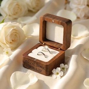 May include: A wooden ring box with two rings inside, one with a large, sparkling stone. The box is engraved with the names "Alice & James" and the date "2026.5.20". The box is open, revealing a white interior.