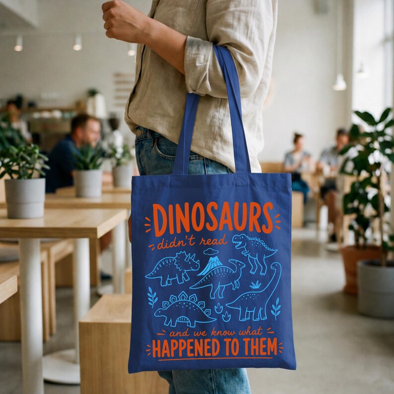May include: A navy blue tote bag featuring orange and blue text and dinosaur illustrations. The text reads "DINOSAURS didn't read and we know what HAPPENED TO THEM". The bag has two navy blue handles.