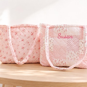 Pu&ograve; includere: Due borse tote trapuntate rosa, con motivi floreali e patchwork. Una borsa ha il nome "Susan" ricamato. Le borse hanno manici coordinati e sono esposte su un tavolo di legno.