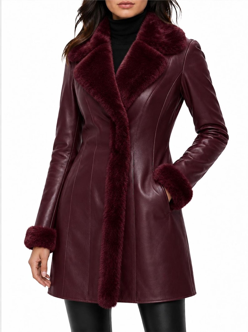 May include: A deep burgundy leather coat featuring a wide faux fur collar, matching faux fur cuffs, and vertical seam detailing. The coat has a structured fit with long sleeves and side pockets, extending to the mid-thigh area.