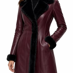 May include: A burgundy leather coat featuring a black faux fur collar and black faux fur cuffs. The coat has a smooth finish, vertical seam detailing, and a long silhouette that extends past the hips, with side pockets integrated into the design.
