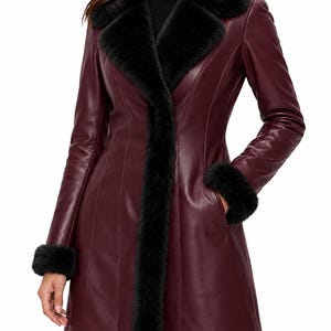May include: A burgundy leather coat featuring a black faux fur collar and black faux fur trim on the cuffs. The coat has a structured fit with vertical seam detailing, long sleeves, and a front opening that extends down to the hemline.