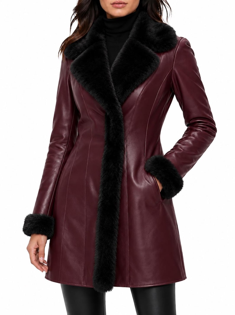 May include: A burgundy leather coat featuring a black faux fur collar and black faux fur trim on the cuffs. The coat has a structured fit with vertical seam detailing, long sleeves, and a front opening that extends down to the hemline.