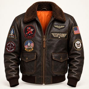 Può includere: Un giubbotto bomber in pelle marrone scuro con colletto in pelliccia sintetica marrone e fodera arancione brillante. La giacca è decorata con varie toppe ricamate, tra cui un logo Top Gun, una bandiera degli Stati Uniti e vari emblemi militari.