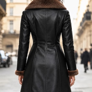 May include: A black leather coat featuring a brown fur collar and brown fur trim on the cuffs. The coat has a fitted waist, long sleeves, and a knee-length hemline, shown from the back view with vertical seam detailing throughout the garment.