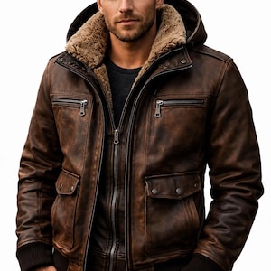 May include: A brown leather bomber jacket featuring a tan faux-fur lined hood, a full-length front zipper, two chest pockets with horizontal zippers, and two lower flap pockets with snap buttons. The jacket has dark brown ribbed cuffs and hem.