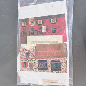 May include: A package containing unassembled holiday-themed baked goods boxes. The boxes feature illustrations of a red house with green shutters and a stone house with Christmas decorations. The words "Merry Christmas" are visible.