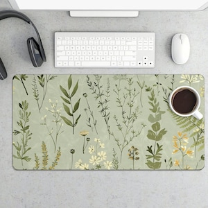 May include: A rectangular desk mat with a light green background and a botanical pattern of various green and yellow plants. A white coffee cup filled with dark liquid sits on the mat, next to a white keyboard and mouse.