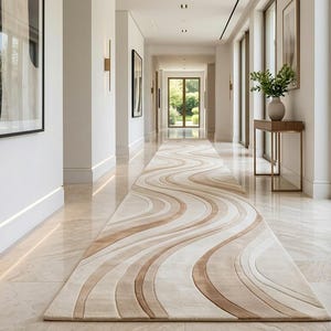 Könnte beinhalten: Ein langer, rechteckiger Läufer mit einem fließenden, wellenförmigen Muster in Creme-, Beige- und Hellbrauntönen. Das Design besteht aus glatten, geschwungenen Linien, die sich über die gesamte Länge des Teppichs erstrecken und Tiefe erzeugen.