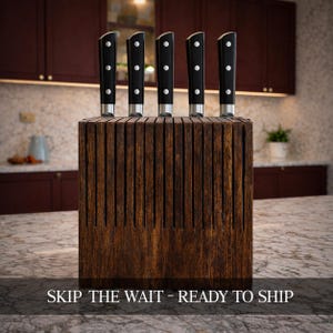 Puede incluir: Un juego de cinco cuchillos de cocina con mangos negros y hojas plateadas, exhibidos en un bloque de cuchillos de madera oscura. El bloque tiene ranuras verticales para cada cuchillo. El texto "SKIP THE WAIT - READY TO SHIP" está en la parte inferior.