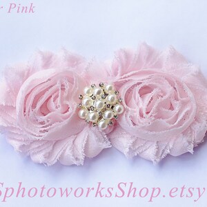 May include: A pink headband with two pink fabric flowers and a pearl and rhinestone embellishment. The headband is made of elastic.