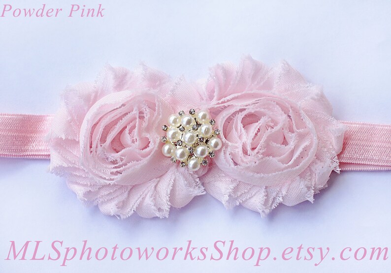 May include: A pink headband with two pink fabric flowers and a pearl and rhinestone embellishment. The headband is made of elastic.