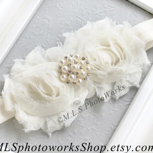May include: White fabric headband with two large white fabric roses and a pearl and rhinestone embellishment.  The headband is made of a soft, stretchy material.