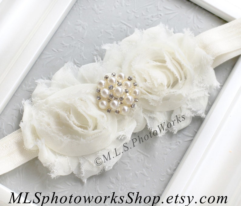 May include: White fabric headband with two large white fabric roses and a pearl and rhinestone embellishment.  The headband is made of a soft, stretchy material.