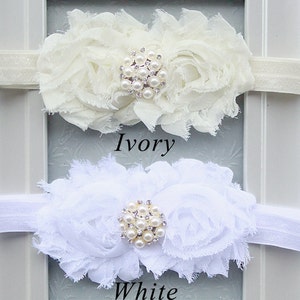 May include: Two white flower headbands with pearl and rhinestone embellishments. The headband on top is ivory and the headband on the bottom is white. The text "Ivory" is below the top headband and the text "White" is below the bottom headband.