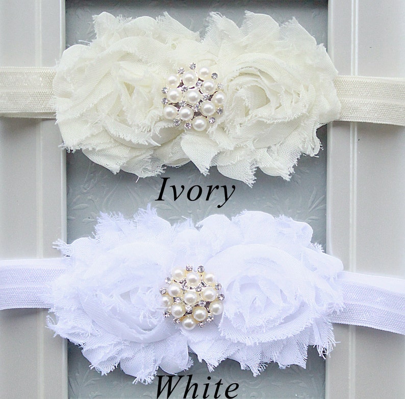 May include: Two white flower headbands with pearl and rhinestone embellishments. The headband on top is ivory and the headband on the bottom is white. The text "Ivory" is below the top headband and the text "White" is below the bottom headband.