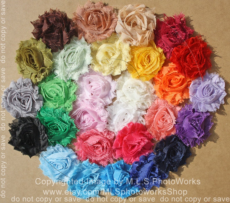 May include: A collection of 20 handmade fabric flowers in various colors, including brown, green, light green, yellow, orange, red, pink, white, blue, and purple. The flowers are arranged in a circle on a brown surface.