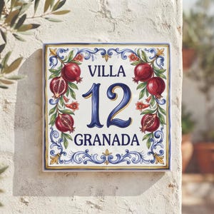Może przedstawiać: Kwadratowa ceramiczna tabliczka na dom z napisem VILLA 12 GRANADA ciemnoniebieskimi literami. Wzór zawiera ręcznie malowane czerwone granaty, zielone liście oraz niebiesko-żółte zawijasy na białym tle z niebieską obwódką.