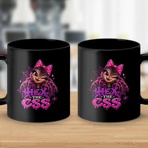 May include: Two black ceramic mugs featuring a graphic of a cartoon spider with a pink polka-dot bow. The spider has large purple eyes and is winking. Below the spider, the text reads "HEX THE CSS" in a stylized, dripping pink font.