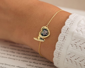 May include: A gold-toned chain bracelet featuring a small, heart-shaped locket charm. The locket is open, revealing a miniature photograph of two people inside. The bracelet is constructed with delicate metal links and a secure clasp mechanism.