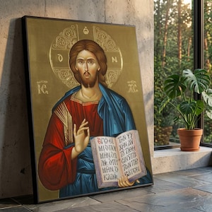Può includere: Icona religiosa incorniciata raffigurante una figura con un'aureola, che indossa vesti rosse e blu, che tiene in mano un libro con testo greco. L'opera d'arte ha uno sfondo dorato ed è esposta all'interno vicino a una finestra con una pianta in vaso.