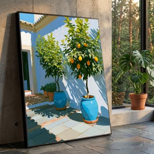 May include: A framed wall art print depicting a sunlit Mediterranean courtyard with two potted lemon trees in vibrant blue ceramic planters. The scene features light-coloured stone tiles, a white wall, and deep shadows cast by the trees.