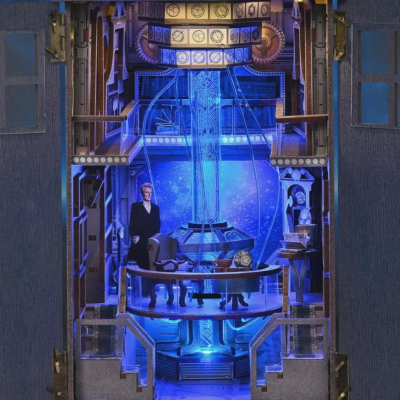 May include: A detailed diorama featuring a figure in a black suit standing in a futuristic interior with blue lighting. The scene includes a central column with glowing energy, a round table, and various architectural elements.