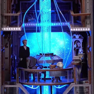 May include: A detailed diorama featuring a figure in a black coat standing in a futuristic interior with blue neon lighting. The scene includes a control panel, a starry backdrop, and the word "FLOW".