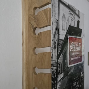 May include: A vertical light brown wooden wall rack featuring five evenly spaced circular cutouts with narrow slots extending to the edge, designed for holding items. The natural wood grain is visible throughout the rectangular structure.