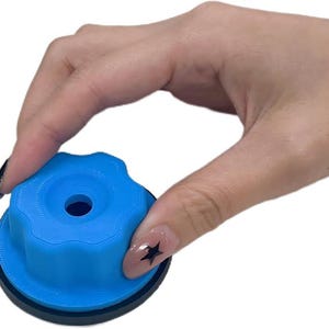 May include: A blue, circular object with a ridged top and a central hole. The object has a black base and is held by a hand with a star-shaped nail design. The object appears to be a knob or a similar component.