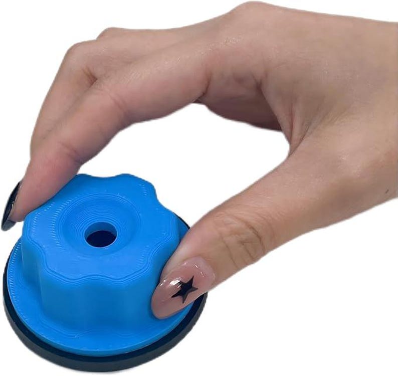 May include: A blue, circular object with a ridged top and a central hole. The object has a black base and is held by a hand with a star-shaped nail design. The object appears to be a knob or a similar component.