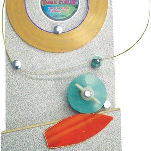 May include: A collage of abstract shapes and a circular design. The design includes a gold-colored circle with a purple inner ring, a teal disc with a white handle, and an orange, leaf-shaped element. The text "TABLE FOLDER" is visible.
