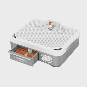 May include: A gray and white glass grinder with a pull-out drawer. The top has a white mesh surface with a handle and an orange water spout. The drawer is open, revealing a sponge and a cylindrical object. The text "THE GRINDER 2" is on the drawer.