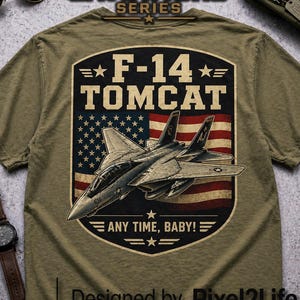 Könnte beinhalten: Olivgrünes T-Shirt mit einer Grafik eines F-14 Tomcat-Kampfjets vor einer amerikanischen Flagge. Das Design enthält den Text "F-14 TOMCAT" und "ANY TIME, BABY!". Teil der Aviation Series.