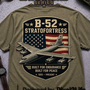 May include: Olive green t-shirt featuring a graphic of a B-52 Stratofortress bomber with an American flag background. Text includes "B-52 Stratofortress", "Built for Endurance, Built for Peace", and "1955-Present".