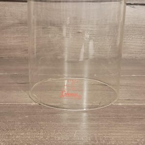 Puede incluir: Un globo cilíndrico de vidrio transparente para linterna con el logotipo rojo de Pyrex y el logotipo rojo de Coleman impresos en la parte frontal. El vidrio es transparente con un acabado liso, abierto por arriba y por abajo.