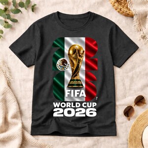 Pu&ograve; includere: Una t-shirt nera a maniche corte con una grande grafica del trofeo della Coppa del Mondo FIFA centrata su una bandiera messicana verticale verde, bianca e rossa. Il numero 2026 &egrave; integrato nel design, con il testo FIFA WORLD CUP 2026 sottostante.