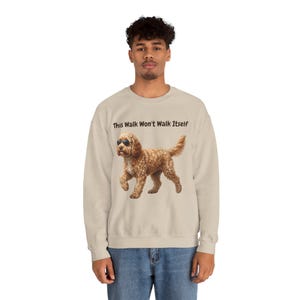 Könnte beinhalten: Beiges Sweatshirt mit dem Text "This Walk Won't Walk Itself". Das Sweatshirt zeigt eine Grafik eines braunen Hundes mit Sonnenbrille. Der Hund geht nach vorne. Das Sweatshirt ist ein lässiger Stil.