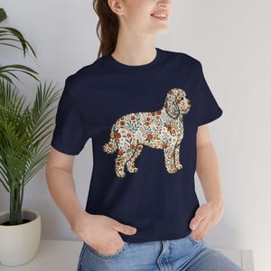 Op de afbeelding: Marineblauw T-shirt met een bloemenhond ontwerp. Het silhouet van de hond is gevuld met rode, oranje en groene bloemen en bladeren. Het shirt heeft een ronde hals en korte mouwen.