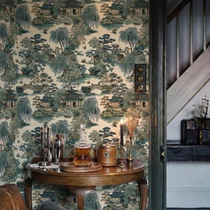 May include: A room with wallpaper featuring a scenic Asian landscape in shades of blue and green. A round wooden table displays a decanter, bar tools, and a candle holder. The room's entrance leads to a staircase.
