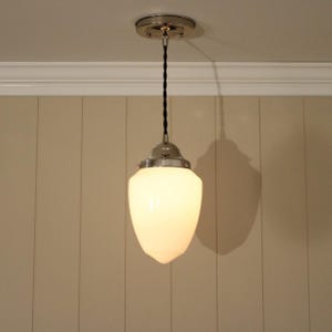 May include: A pendant light fixture featuring a smooth, opaque white glass shade with a teardrop shape. The shade is attached to a polished nickel metal cap and suspended by a black twisted fabric cord from a matching circular ceiling canopy.