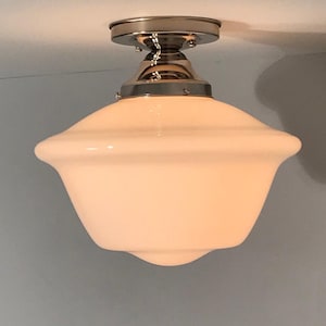 May include: A semi-flush mount ceiling light fixture featuring a smooth, opaque white glass schoolhouse-style shade. The shade is attached to a polished chrome metal canopy and fitter, which connects the glass globe to the ceiling surface.