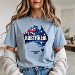 以下が含まれることがあります： オーストラリアの地図が描かれた水色のTシャツ。オーストラリアの国旗と「AUSTRALIA」の文字がプリントされています。シャツには「Aussie Aussie Aussie, Oi Oi Oi!」の文字も含まれています。