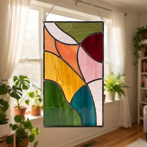 Pode incluir: Um painel retangular de vitral com uma composição abstrata de formas curvas e entrelaçadas em tons de verde-oliva, vermelho escuro, rosa suave, laranja brilhante, amarelo dourado, azul-petróleo e branco, unidas por linhas de chumbo escuras.