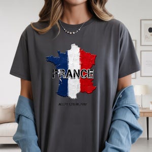 以下が含まれることがあります： フランスの国旗の色（青、白、赤）で描かれたフランスの地図が特徴のダークグレーのTシャツ。「FRANCE」の文字が地図の上にプリントされています。地図の下には「ALLEZ LES BLEUS！」と書かれています。