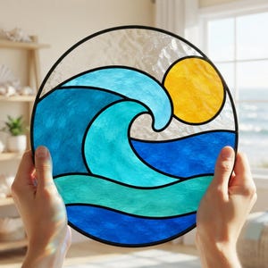Puede incluir: Un atrapasoles circular de vidrieras que presenta una ola oceánica estilizada en tonos azul claro y oscuro, contrastada por un sol amarillo brillante sobre un cielo de vidrio transparente texturizado, unido por líneas de plomo negras.
